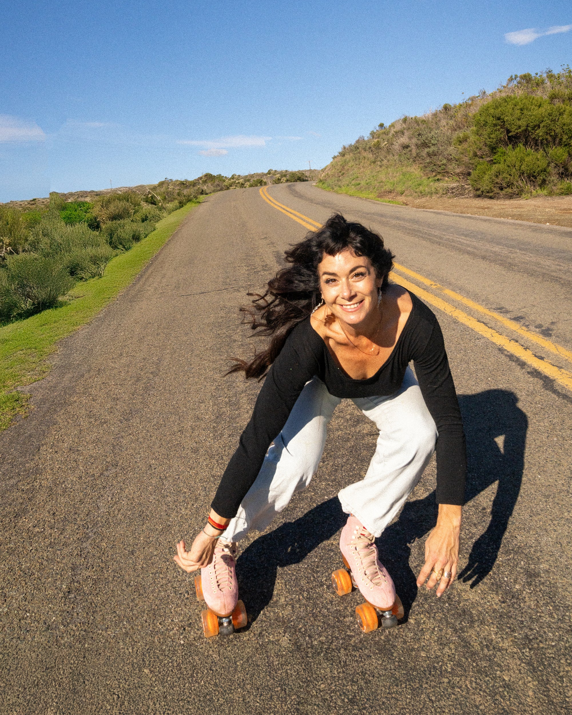 Woman roller skating on a road with greenery and blue sky in the background